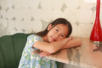Smiling Asian girl child age about 9 years old sit on sofa chair and lying on marble table with looking camera. - 761952083