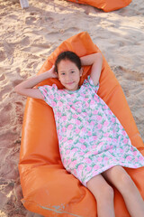 Portrait of smiling Asian young girl relax on sofa bed beach on sand at summer holiday. - 761953297