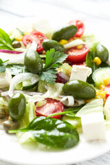 Healthy Salad with Feta Cheese, Green Olives, Baby Spinach, Cucumber, Cherry Tomatoes and Capers. Bright background. Close up.	