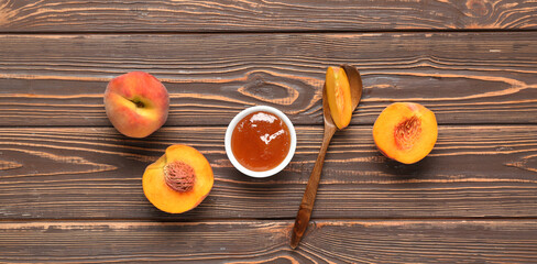 Bowl of sweet peach jam, spoon and fresh fruit on wooden background, top view