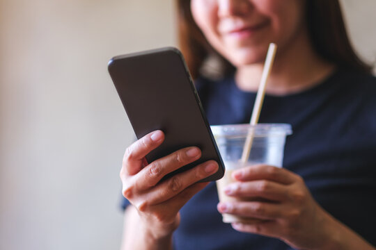 Closeup image of a young woman drinking coffee while chatting on mobile phone