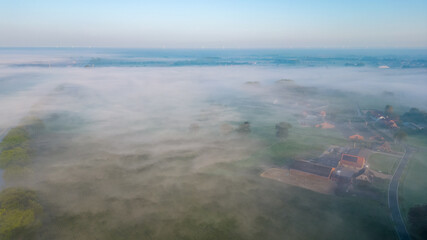 This image offers an aerial view of a misty countryside at sunrise. The soft morning light gently...