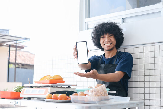 Young Asian man vegetables seller showing blank screen phone for mockup with happy expression