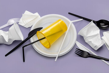 Used plastic utensils, crumpled disposable cups and paper napkins on a lilac background. Plastic recycling.