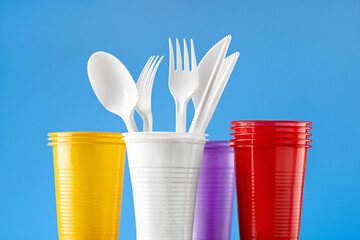 Disposable multi-colored plastic cups and cutlery on a blue background. Ecology and recycling concept.