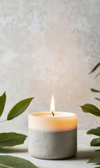 Obraz na płótnie Canvas Natural wax candle in concrete cement holder with green leaves on light background. Minimalist modern design. Stylish decoration for banner, flyer, poster or postcard with copy space.