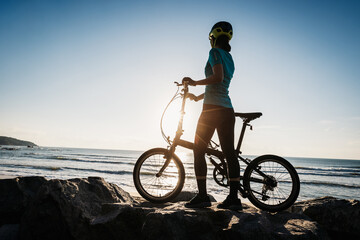 Fototapeta na wymiar Woman taking a folding bike on sunrise seaside