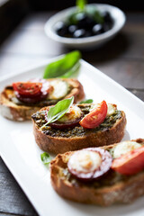 Crostini with tomato, salami and olive pesto on wooden background.