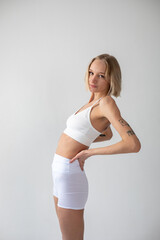 Blonde girl posing on a white background in a top and leggings