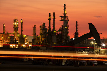 Evening traffic passes by an oil pump jack and refinery in Bakersfield, California, USA at sunset. - obrazy, fototapety, plakaty