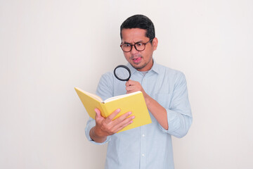 Adult Asian man searching something inside a book using magnifying glass