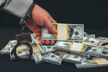 Close-up of a handcuffed hand reaching for money on a black background. A hand in a shirt and...