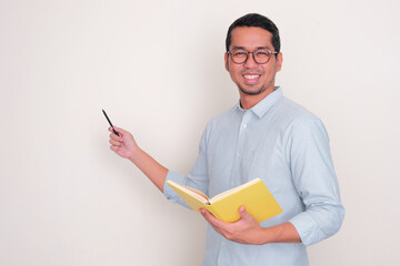 A lecturer smiling at the camera while holding a book and pointing beside