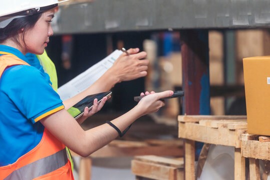 Warehouse management team check stock inventory. Asian men women worker use bar code scaner scan goods shelf writing checklist on clipboard. Teamwork logistics staff counting products store inventory