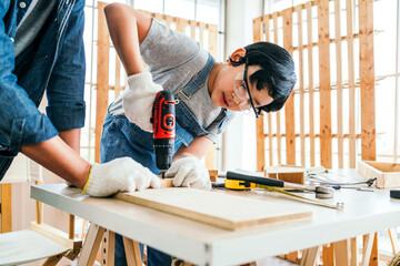 Asian father and son work as a woodworker or carpenters. Close up hands of the father and his son drill holes in a wooden plank carefully together. carpentry working at a home workshop studio. - 762032040