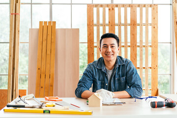 Portrait of a smile Asian male father sitting and working on the table with the instrument of measure and working tools on the table at home woodwork studio. - 762032223