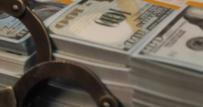 Maximum close-up. Stacks of money packed with bank tape with handcuffs on a black background. Money lies next to handcuffs on a black background. Concept of bribery, corruption.