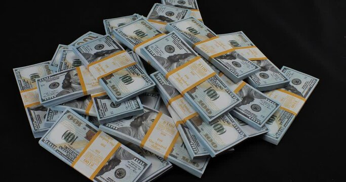 There is a stack of dollars on a black background, more money is thrown into it, and at the end handcuffs fall down. Handcuffs fall on a stack of hundred dollar bills on a black background.