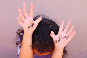 A toddler girl sits with her head down with her hands above her head, where her palms say stop...