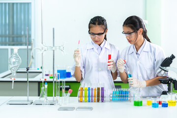 Two Asian female doctors and scientists dripping solution with test tubes, beakers, droppers, measuring cylinders and microscopes. Make medicine, medical and pharmaceutical industry business.