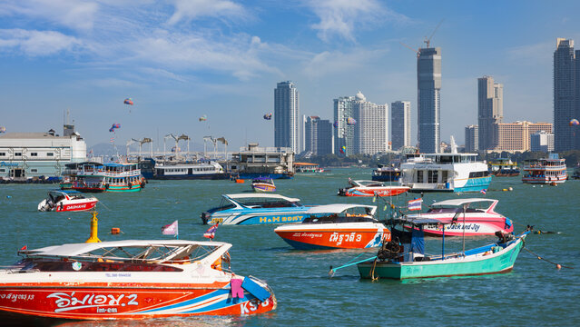 Pattaya, Thailand - 21 December, 2023: View with numerous colorful speed boats and ferries against the backdrop of modern skyscrapers in Pattaya, Thailand. Active leisure on a tropical summer vacation