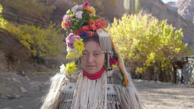 Smiling old Indigenous tribal woman wearing fancy attire with colourful floral crown on head looking at camera on the occasion of religious ceremony in Aryan village called Darchik in Upper Himalayas