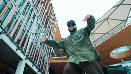 Low angle view of hipster pose in hip hop style surrounded by mall view. Portrait of sporty asian hip hop choreographer dancing break dance while looking at camera. Outdoor sport 2024. Endeavor.