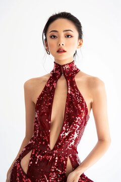Portrait of a pretty young woman super model of Chinese ethnicity donning a glamorous red sequined dress with a high neckline, open back, and thigh-high slit