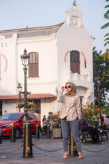 happy asian muslim woman wearing sunglasses and standing beside the street roaming around kota lama or old city area, Semarang, Central Java , Indonesia. Traveling concept