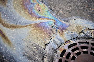 The oil slick on the asphalt road is contributing to water pollution as it drains into the storm drain.