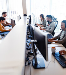 In their office, a multi-ethnic group of IT professionals works together, collaborating and using computers to accomplish their tasks - 762076435