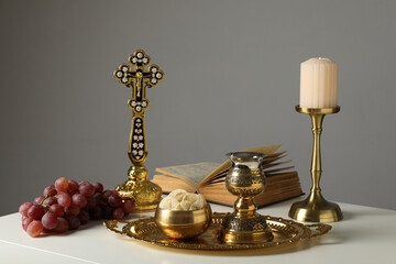 Candle, book, grapes, liturgical bread, golden cross and cup on table on gray background