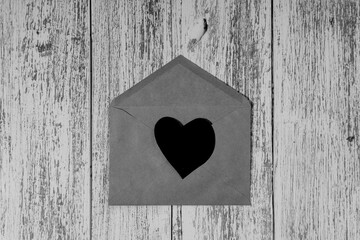 Paper black heart on envelope on wooden table. Black and white image. Concept of unrequited love, divorce