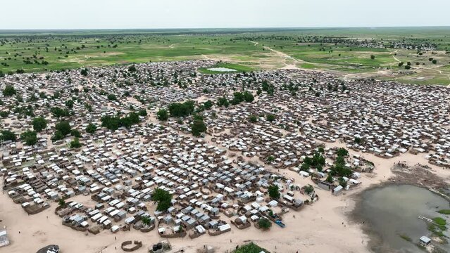 Static high-angle shot of makeshift Nigerian refugee town with oasis near meadow