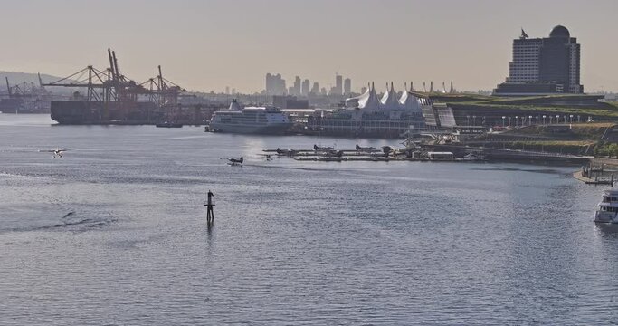 Vancouver BC Canada Aerial v87 zoomed view drone flyover the harbour capturing seaplane landing on the water against shipyard and waterfront downtown cityscape - Shot with Mavic 3 Pro Cine - July 2023