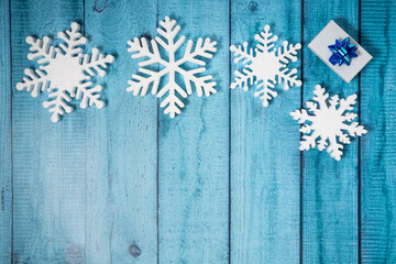 Snowflakes and a present with blue ribbon on a light blue wooden background. Christmas winter flatlay with copyspace