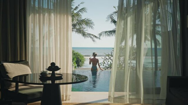 Classy woman drinking wine on infinity pool edge looking at sea in Bali