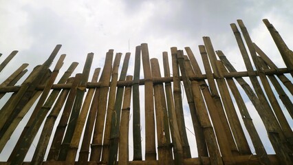 Traditional fence made for bamboo against gray sky, textured background