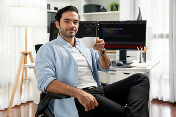 Profile's smart IT developer looking camera to pose holding coffee cup against on software...