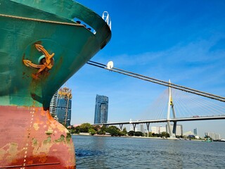 Fototapeta premium ship in the port, Anchor on large cargo ship's anchor being pulled. Green and red ship, While docked at the pier by large ropes on the river, on the building background and transport concept