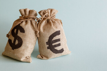 A bag with dollars and a bag with euros on a light background.