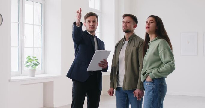 Realtor showing beautiful house to a young happy couple. Professional real estate agent showing new apartment. Successful family ready to become homeowners. Real estate market concept. 4k video.