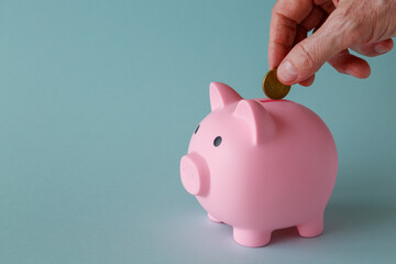 A man's hand drops a coin into a piggy bank. The concept of savings and investments.