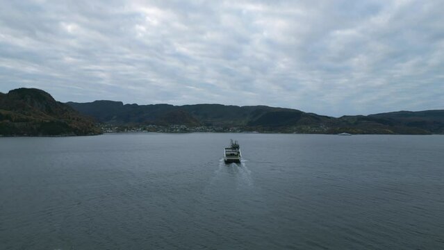 A ferry crossing calm waters near nesvik with hjelmeland backdrop, cloudy skies, aerial view