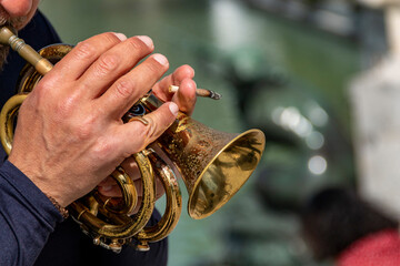 Man's hand playing an old, worn trumpet in an outdoor park while holding a lit cigarette