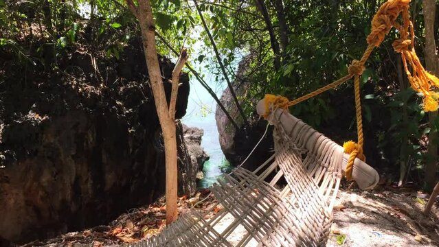 A slow walk past a hammock in the jungle near the beach in Siquijor island. The hammock looks comfortable and it is tied up with an orange rope. The sea view is in the background.