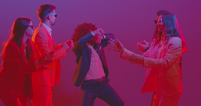 Funny dancer. Crazy young team of people dances at a party illuminated by neon light, dressed in colorful costumes and glasses. Energy of disco music creating a atmosphere of celebration.