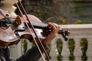 Man's hand playing an old and worn violin in an outdoor park
