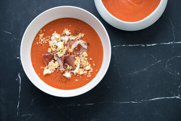 White bowls with salmorejo or spanish tomato and bread soup, top view on a black marble background, horizontal shot with copyspace
