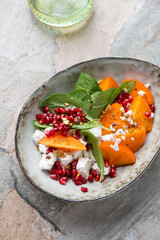 Bowl of persimmon, goat cheese, spinach and pomegranate salad, vertical shot on a grey granite background, elevated view